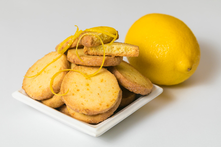 Homemade lemon cookies in a white saucer near fresh lemon on white background. Closeup, isolatedの写真素材