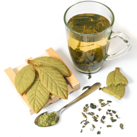 Homemade matcha green tea shortbread cookies in shape of green tea leaves on the wooden stand near green tea cup isolated on white background. Square pictureの写真素材