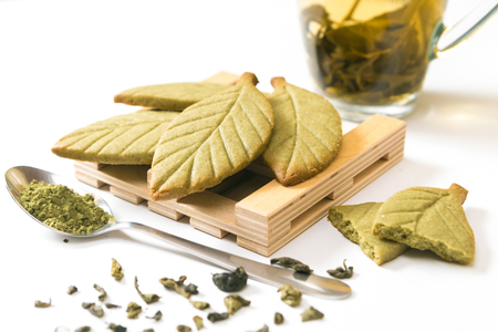 Homemade matcha green tea shortbread cookies in shape of green tea leaves on the wooden stand near green tea cup isolated on white background.の写真素材