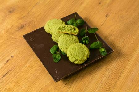 Peppermint Cookies with mint leaves stacked on dark chocolate bar at wooden background