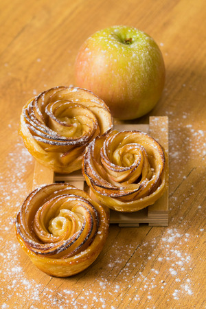 Homemade apple cakes with cinnamon and icing sugar on wooden background. Apple Rose mini tartsの写真素材
