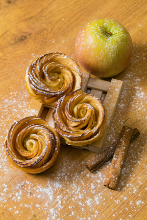 Homemade apple cakes with cinnamon and icing sugar on wooden background. Apple Rose mini tartsの写真素材