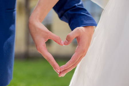 groom with the bride holding hands in the shape of a heart in the parkの写真素材