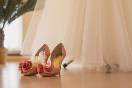 The bride's shoes stand on the floor near the wedding dress in the roomの写真素材