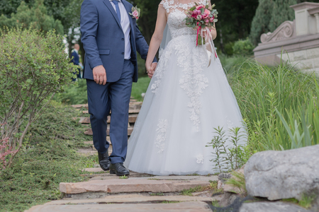 bride and groom walk together by the hand in the parkの写真素材