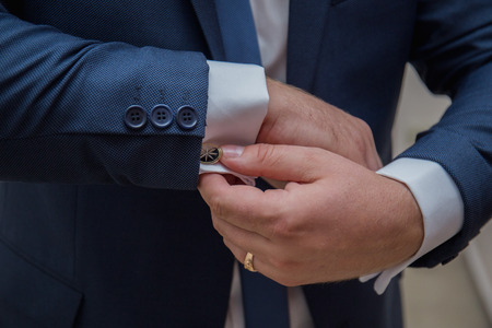 the groom fastens the cuffs of the sleeves on the shirt