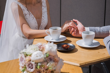 the bride and groom sit at a table in a cafe drinking coffeeの写真素材