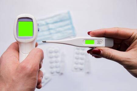 electronic thermometer in hand with a medical maskの写真素材