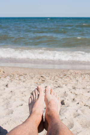 male legs on a deck chair against of seaの写真素材