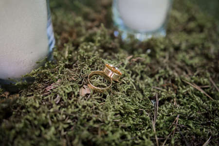 a gold wedding rings on green moss near candlesの写真素材