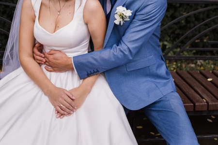 the groom and the bride sit on bench in the park