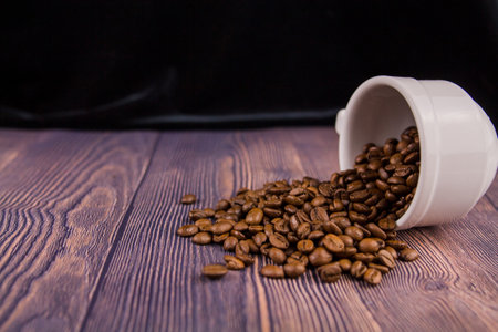 A coffee beans sprinkled from a white cup on a wooden tableの写真素材