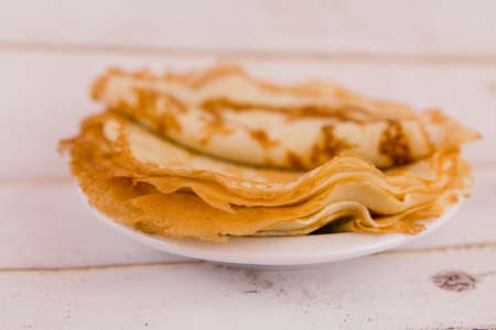 a thin delicious round pancakes on a white plate on a wooden table in the kitchen