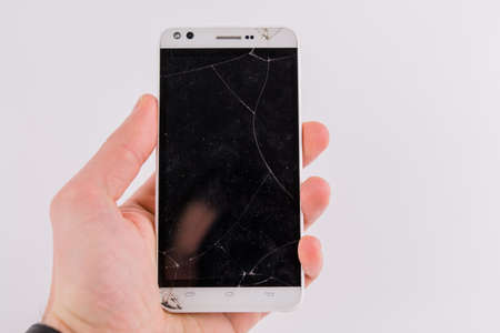 a smartphone with broken screen in hand on white background