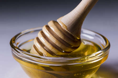a fresh golden honey pours beautifully from a wooden honey spoon
