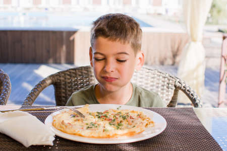 boy eats an omelette on a sandy terrace in a restaurantの写真素材