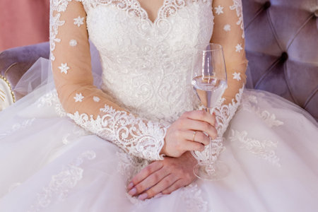 bride in a white wedding dress holds a glass of wine in her handの写真素材