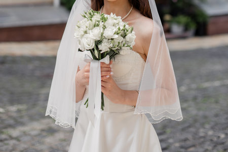bride in a white dress with a wedding bouquet on a city streetの写真素材