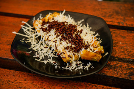 Chocolate eclair on a black plate on a wooden table.