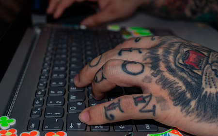 left hand of a tattooed man on the keyboard of a laptop