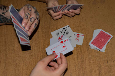 The hands of a man with tattoos and a woman playing cards on a wooden tableの写真素材