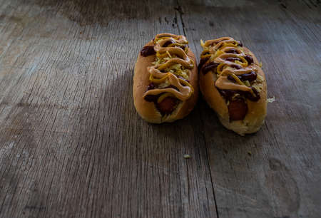 Two hot dogs and french fries with rose, tomato and mustard sauces, in rustic woodの写真素材