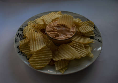 white plate with curly fries with pink sauce in the middle, in a glass bowl, on a white background