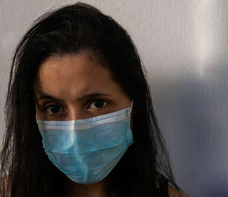 young, white woman with loose black hair, frowning looking directly at the camera, wearing a face mask on a light backgroundの写真素材