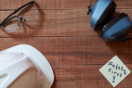 Safety first note one yellow piece of paper stuck on wooden background with full set of personal protective equipment: helmet, safet glasses and ear protection. Safety first concept.の写真素材