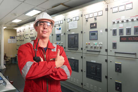 Ship's mechanic near marine diesel generators on a merchant ship in the engine room with all the...