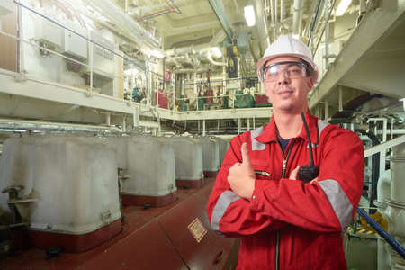 Ship's mechanic near marine diesel generators on a merchant ship in the engine room with all the...