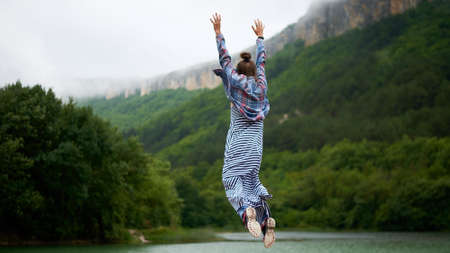 Casual dressed hiking woman under the rain jumping near the lake in mountains. Candid and authentic expression.の写真素材