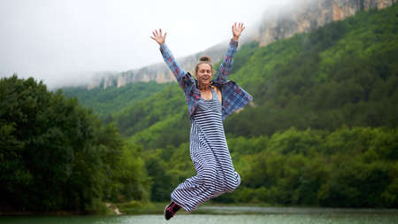 Casual dressed hiking woman under the rain dancing near the lake in mountains. Candid and authentic...