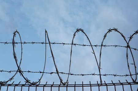 Barbed wire silhouette on a blue cloudy background as a border, privacy, quarantine or security...