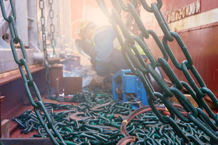 Welder doing welding on deck of ship lashing cargo for sea shipping on background of lenty lashing chains. Cargo securing concept.の写真素材
