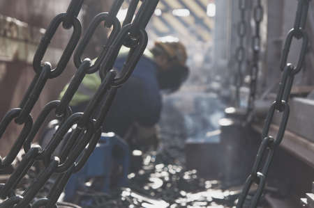Welder doing welding on deck of ship lashing cargo for sea shipping on background of lenty lashing chains. Cargo securing concept.の写真素材