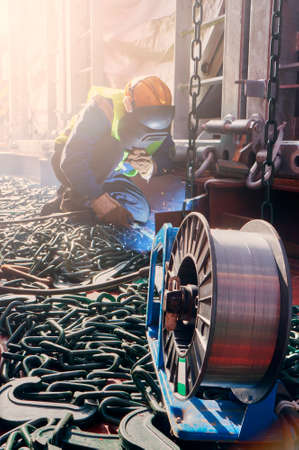 Welder doing welding on deck of ship lashing cargo for sea shipping on background of lenty lashing chains. Cargo securing concept.の写真素材