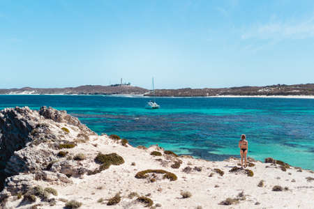 Girl standing alone in an epic beach landscape on Rottnest Island, Perth, Western Australia. The pristine blue water and Rottnest lighthouse in the background make for an iconic shot.のeditorial素材