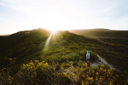 Girl standing alone in the middle of the South Australian bush, watching the golden sun set over the...