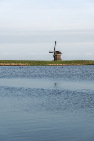 Solitary Mill characterized by its traditional thatched roof at Dutch Lake at Dusk. Half hidden behind a verdant dike overlooking the tranquil water of a flooded meadowの写真素材