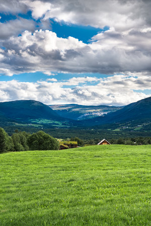 Lush grassland of Oppdal valley, in TrÃ¸ndelag Norway with a farm tucked behind a rolling hill, under a sky filled with striking clouds.の写真素材