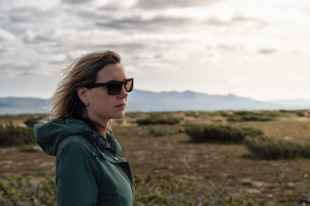 Woman in sunglasses stands in the Flatruet high fell Sweden, facing the majestic mountains, her hair...