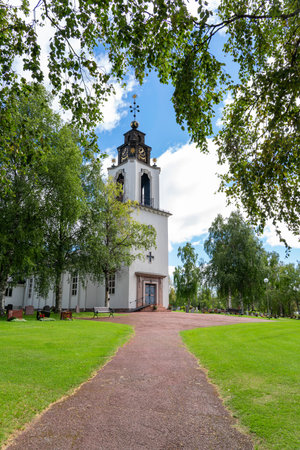 A tranquil day at the Church of Sweden in Idre Dalarna, showcasing the building's architecture amidst green trees under a blue sky and white cloudsの写真素材