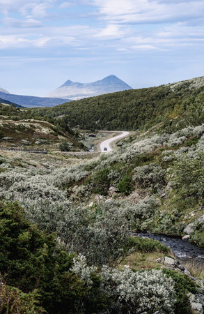 A car driving a winding road surrounded by the rugged terrain of Rondane National Park. Bare...