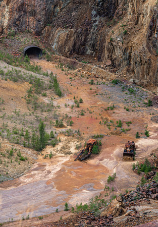 In the former copper mine of Falun Sweden, rusted vehicles lie amid a colorful red soil landscape of...