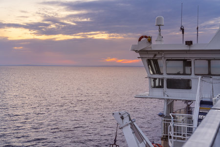 A stunning sunset casts vibrant colors across the sea while the ferry cruise ship sails through the tranquil Kattegat Strait, with the bridge in view.の写真素材