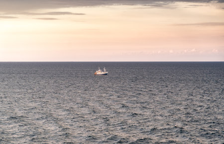 Sunrise breaks over the Skagerrak North Sea in Sweden. A lone shrimp trawler appears on the water, fishing near the coast between Norway and Sweden.の写真素材