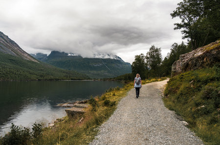 lone female hiker with backpack on a gravel trail in innerdalen, norway. moody autumn landscape with...