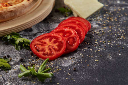 Whole and cutted tomato in ingredients of pizza on italian black paper tableの写真素材