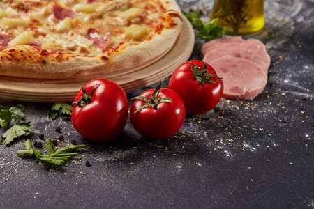 Whole and cutted tomato in ingredients of pizza on italian black paper tableの写真素材